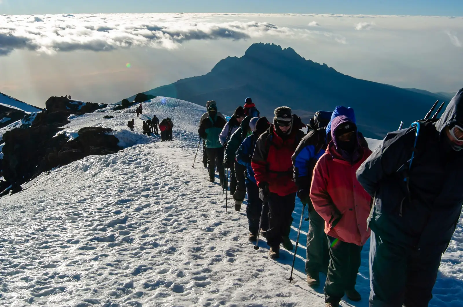 Climbers on the snowy crater rim at sunrise, with Mawenzi peak behind