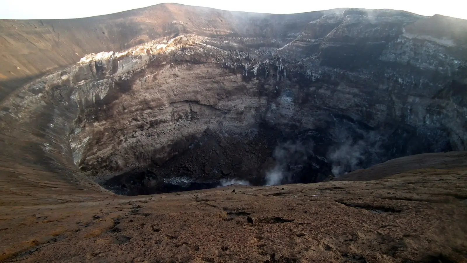 The deep summit crater of Ol Doinyo Lengai seen from the rim, with steam rising
