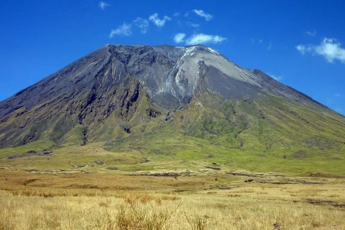 The cone of Ol Doinyo Lengai above green grassland