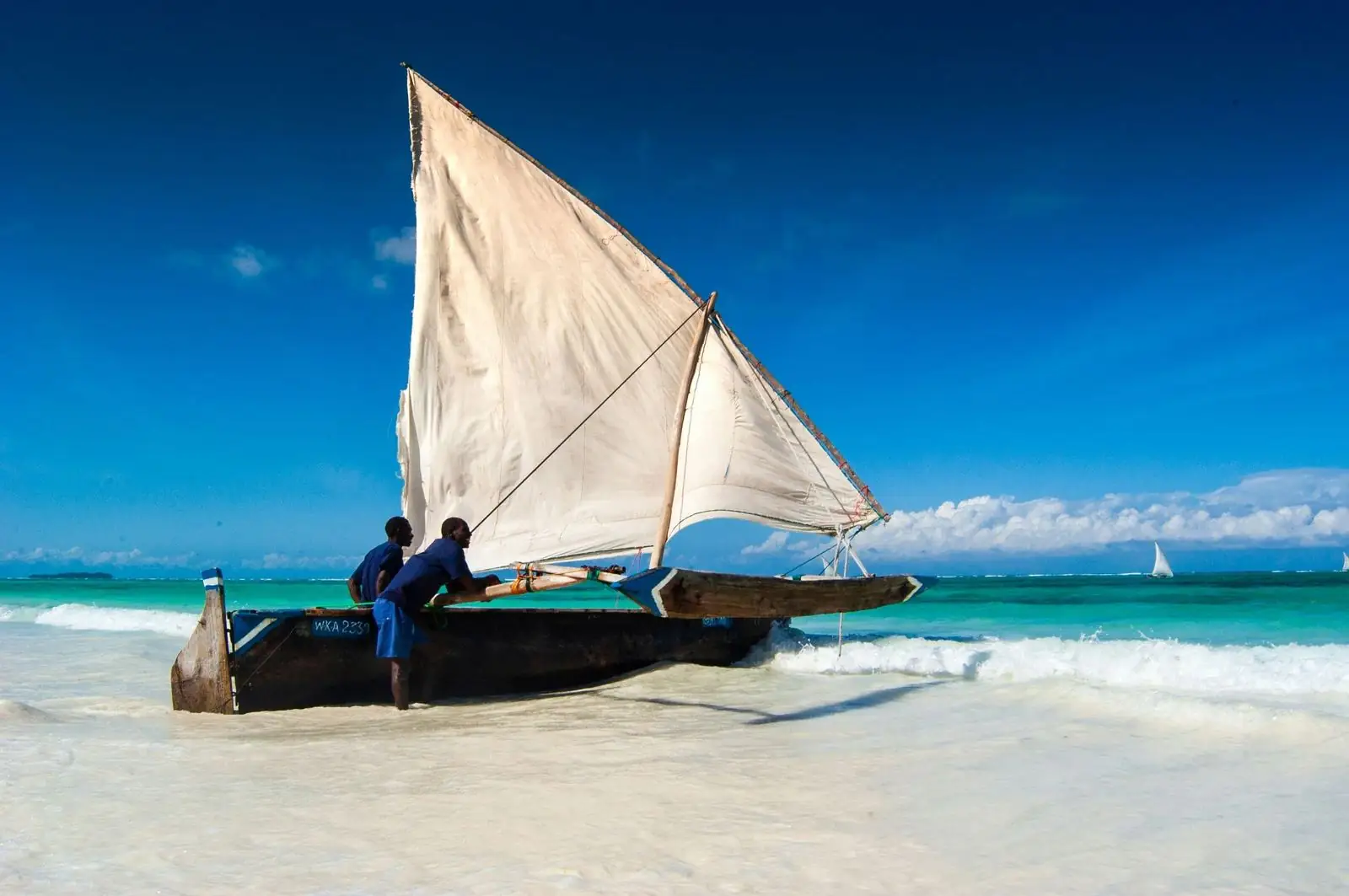 A traditional dhow on a white beach with turquoise water