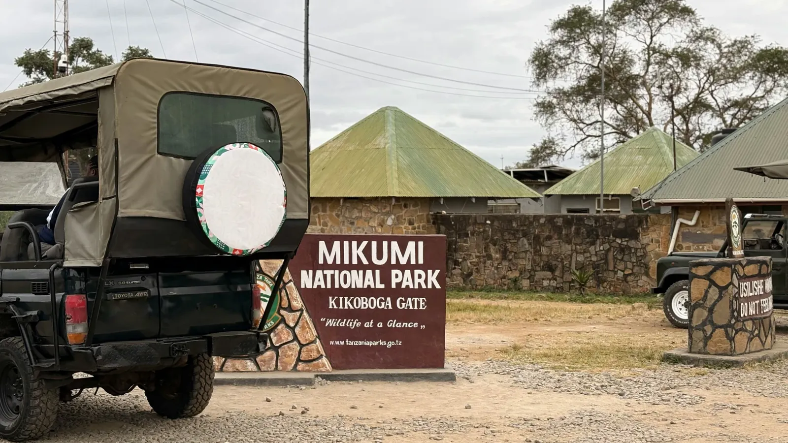 A safari vehicle parked beside the Mikumi National Park sign at Kikoboga Gate